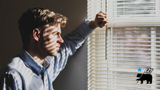 Man peering through window blinds, waiting for his bike to be delivered.